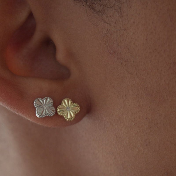 Close-up of a person wearing gold and silver clover earrings.