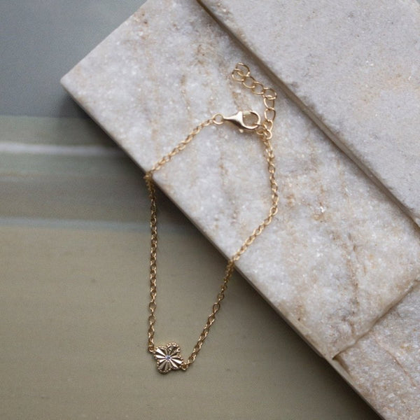 Gold bracelet with a clover-shaped clasp on a marble surface