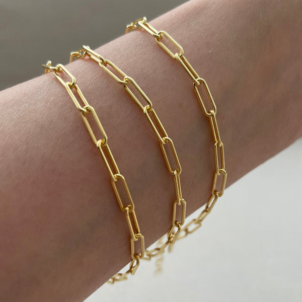 Gold chain bracelets on a wrist against a neutral background