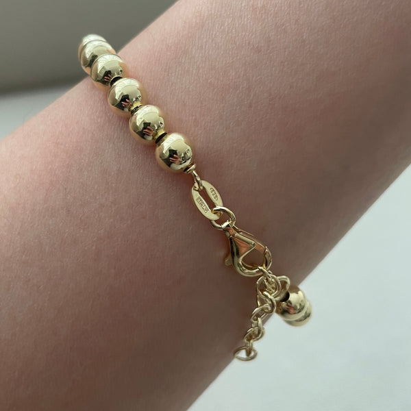 Gold bracelet on a wrist against a neutral background