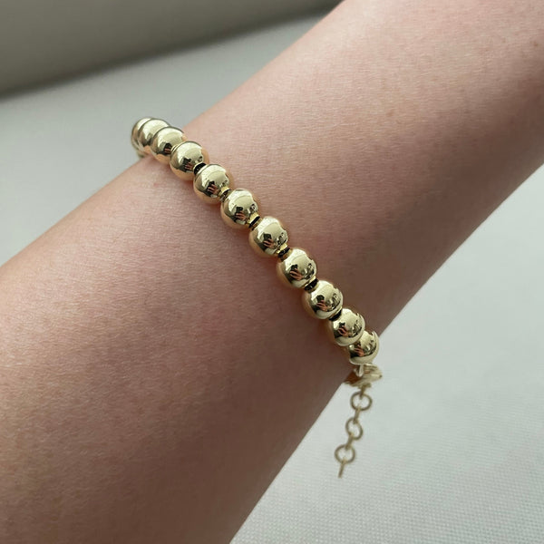 Gold beaded bracelet on a wrist against a neutral background