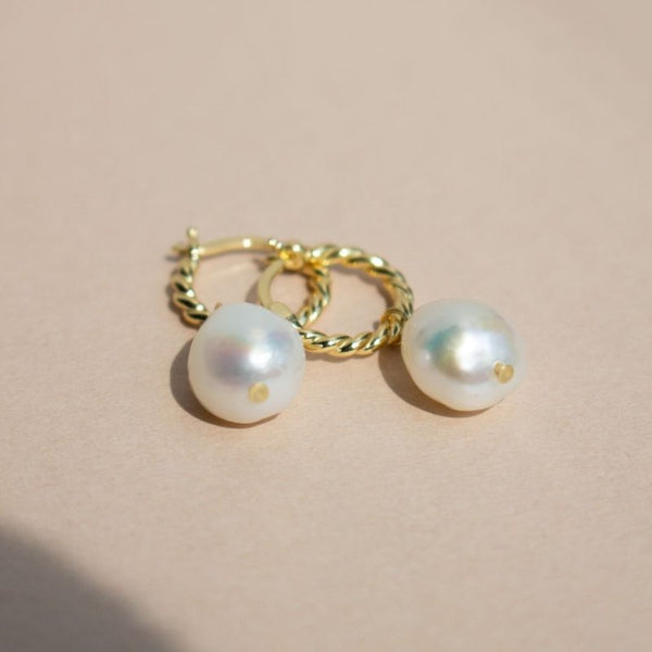 Pearl earrings with gold hooks on a beige background