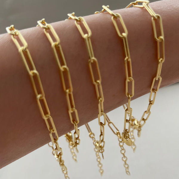 Gold chain bracelets on a wrist against a neutral background