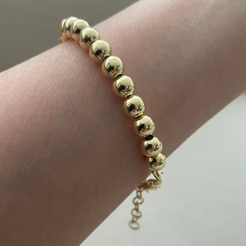 Gold beaded bracelet on a wrist against a neutral background