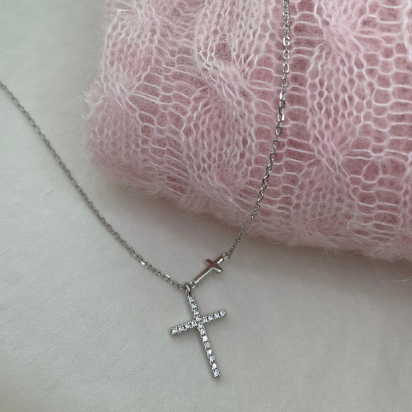 Silver necklace with a cross pendant on a pink lace fabric background