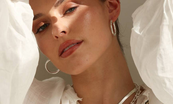 Close-up of a person wearing silver hoop earrings and a necklace with a white background