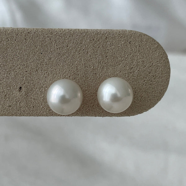Two pearl earrings on a textured beige stick against a white fabric background