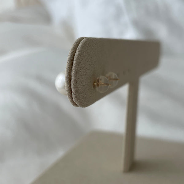 Gold earrings on a white stand with a blurred white background