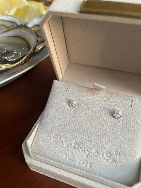 Pearl earrings with cubic zirconia in a velvet white box embossed with "Sisterberry & Co. Est. 2020" with fresh oysters and lemon in the background.