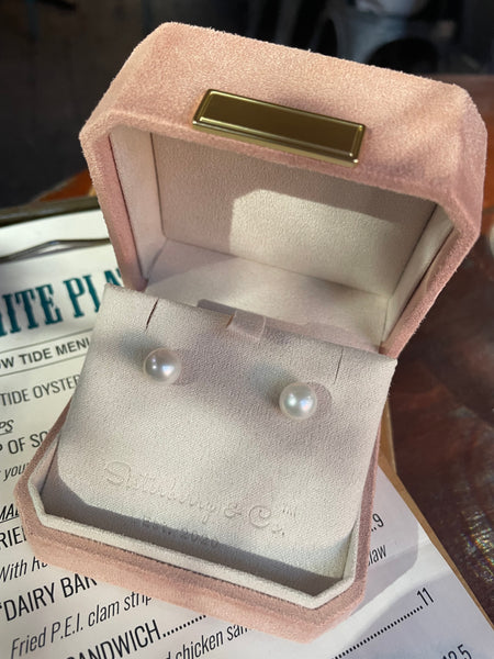 Pair of pearl earrings in a velvety blush pink jewellery box embossed with 'Sisterberry & Co., Est 2020" place on top of a clipboard seafood menu