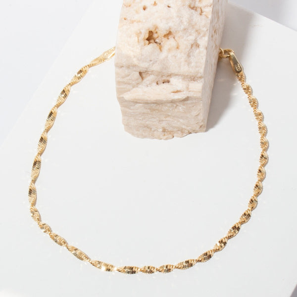 Gold chain necklace on a white surface with a textured block