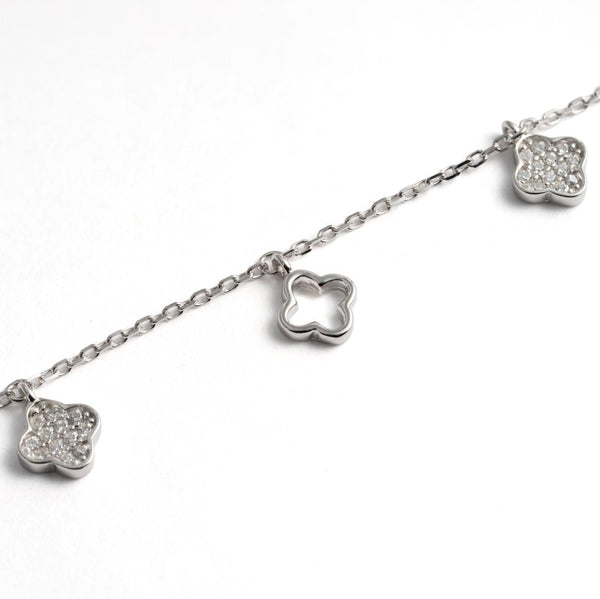 A silver chain bracelet featuring three clover-shaped charms, including two pavé-set clear stones and one open metal clover charm, on a white background.