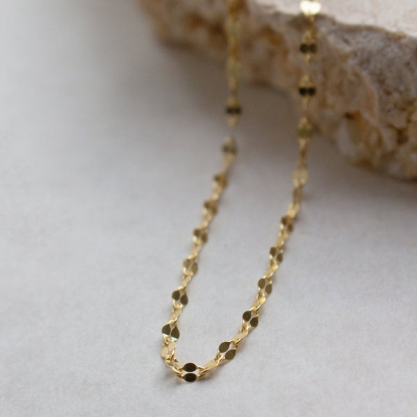 Gold chain necklace on a light gray surface with a neutral background