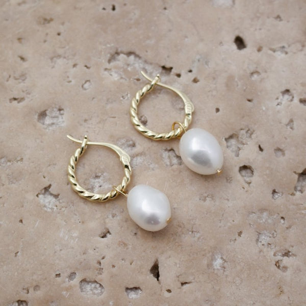 Gold hoop earrings with white pearls on a textured beige surface