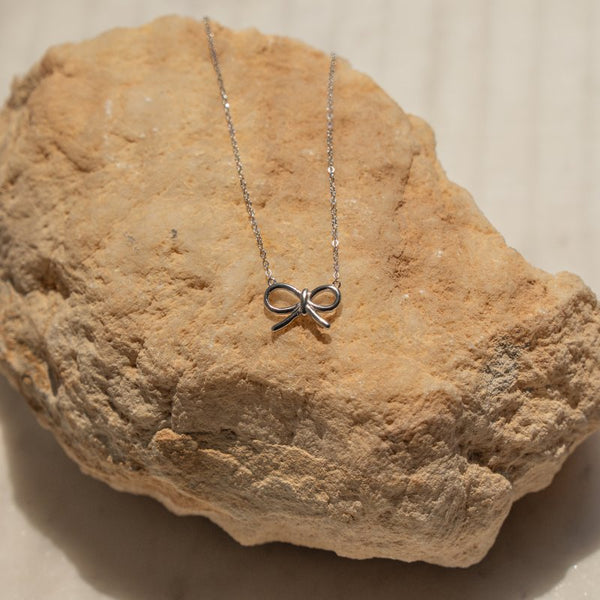 Silver bow-shaped necklace on a textured stone surface
