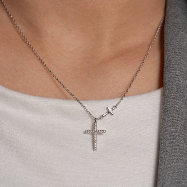 Silver cross necklace worn by a person with a neutral background
