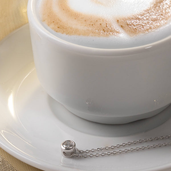 Silver necklace with a small round diamond bezel pendant on a coffee plate