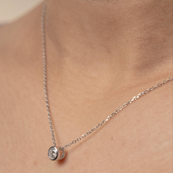 Silver necklace with a small round diamond bezel pendant on a woman