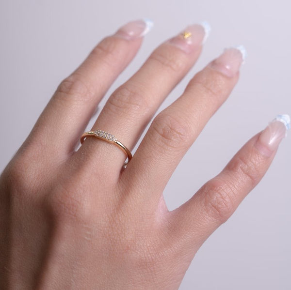 Hand wearing a gold ring with a clear gemstone on a light gray background