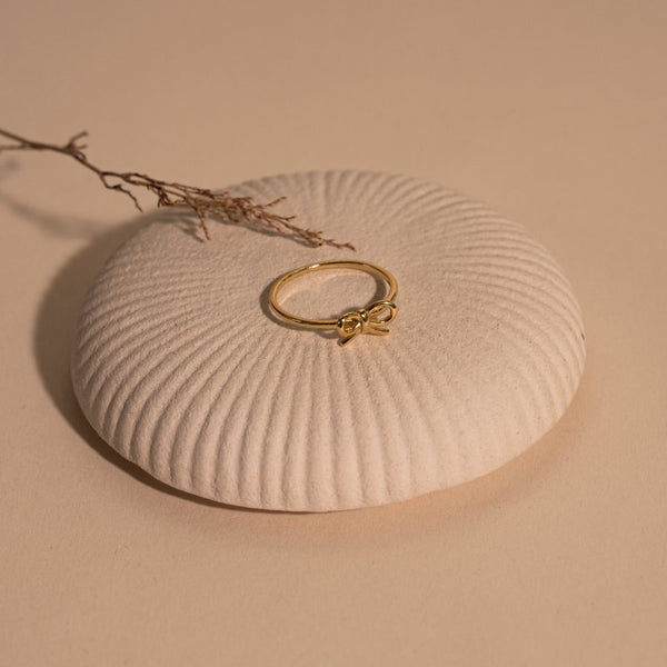 Gold ring with a bow design on a textured beige surface