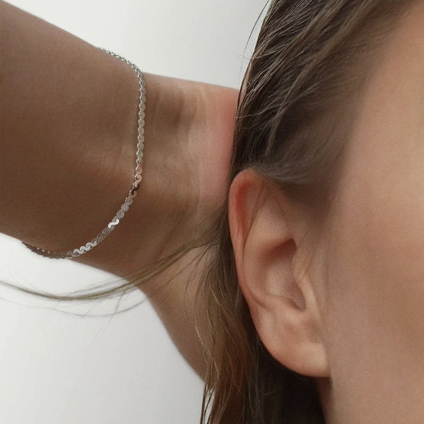 Close-up of a person wearing a delicate silver chain bracelet on their wrist.