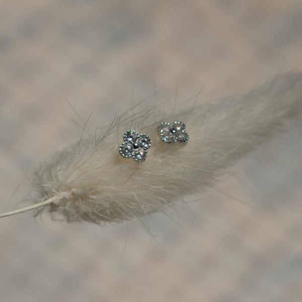 Silver floral earrings on a dried grass stem with a blurred natural background